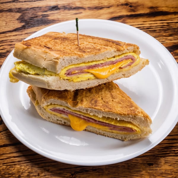 Two halves of a grilled breakfast sandwich with egg, ham, and melted cheese on a white plate.