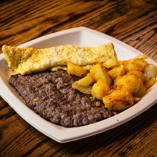 Breakfast plate with a folded omelet, sausage patty, and roasted potatoes on a wooden table.