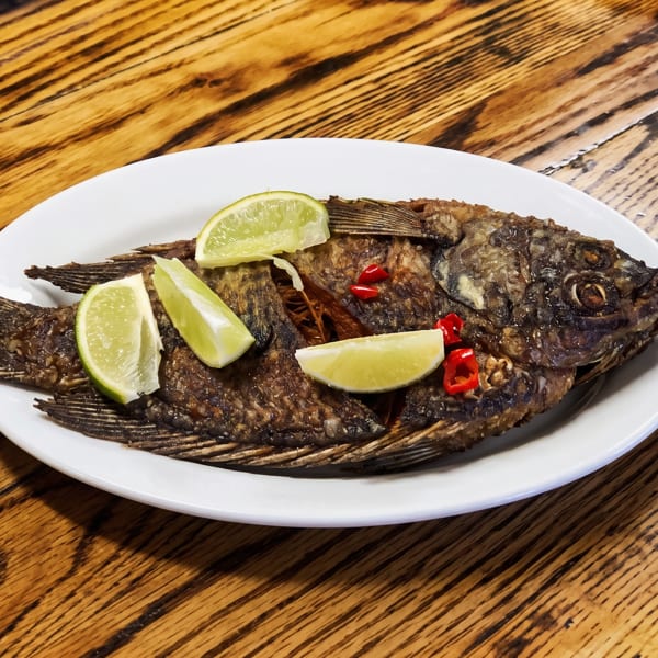 Whole fried fish garnished with lime wedges and red chili peppers on a white plate.